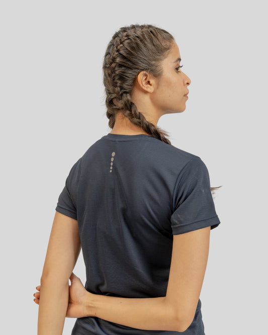 Person wearing a dark gray t-shirt with a small logo on the back, standing against a light gray background.