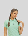 Woman wearing a light green polo shirt with braided hair against a plain background
