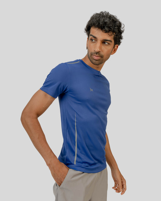 Man wearing a blue athletic shirt and gray shorts on a light gray background