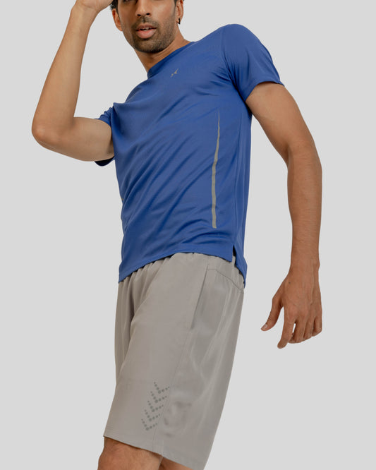 Man wearing a blue athletic shirt and gray shorts on a light gray background
