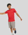 Man wearing a red athletic shirt and gray shorts on a light gray background