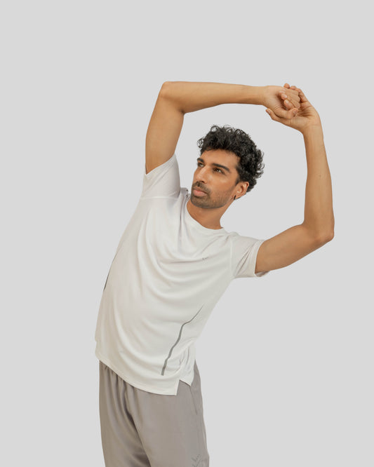 Man in a white t-shirt and gray pants stretching against a light gray background
