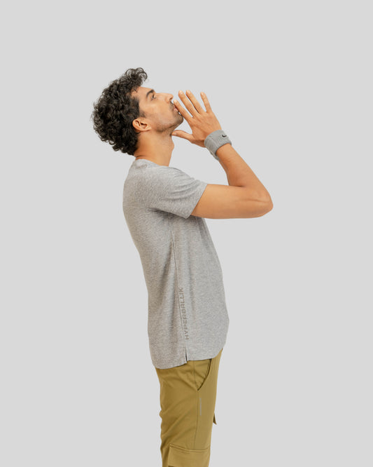 Man in gray shirt and beige pants covering his mouth with his hand on a light gray background