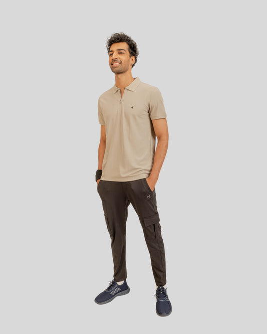 Man wearing a beige polo shirt and dark cargo pants on a light gray background