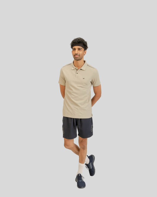 Man wearing a beige polo shirt and black shorts on a light gray background