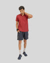 Man wearing a red polo shirt and dark shorts on a light gray background