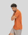 Man wearing an orange polo shirt and gray shorts on a light gray background