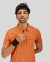 Man wearing an orange polo shirt with a brand logo on a gray background