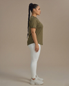 Woman wearing an olive green t-shirt and white pants against a beige background