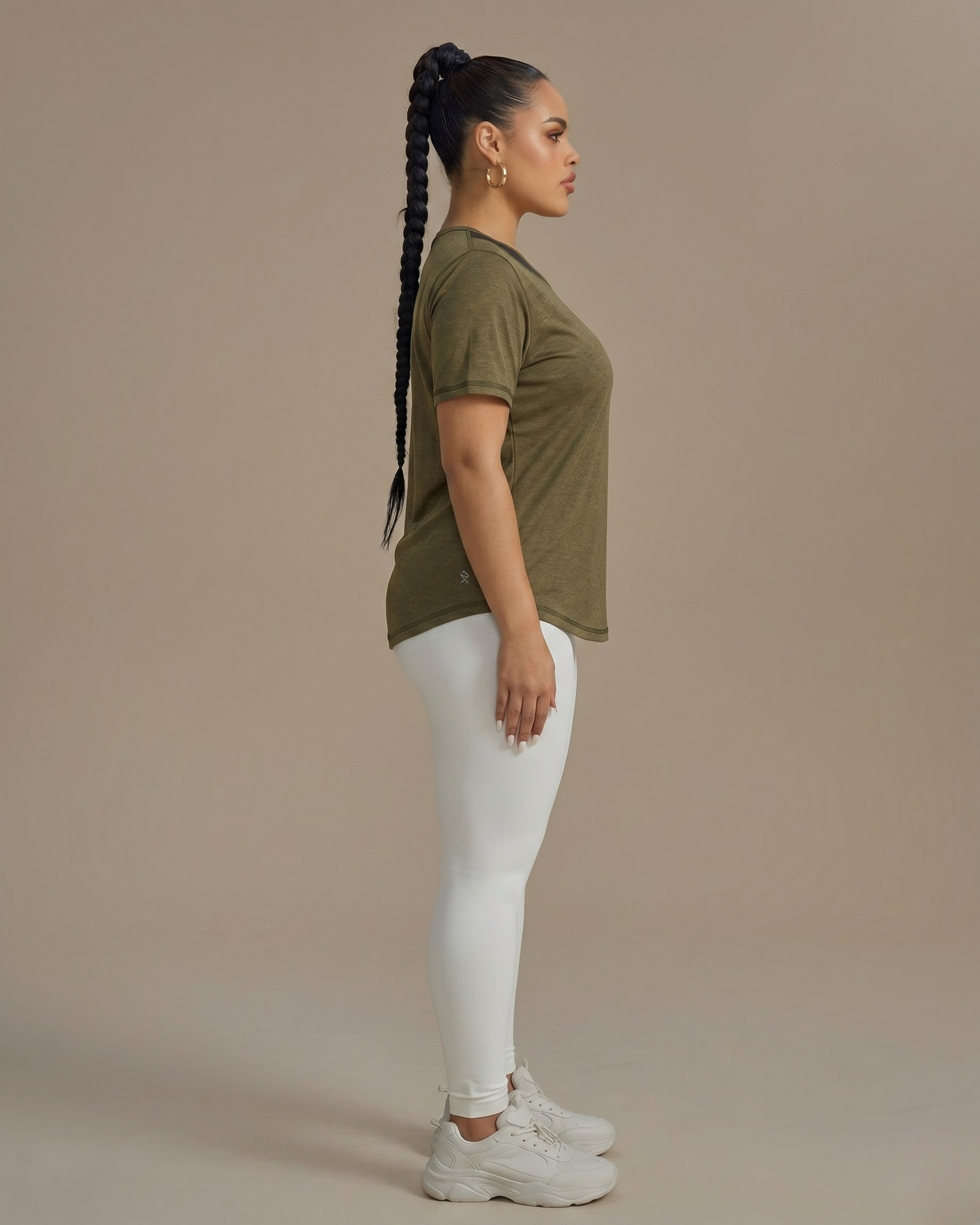 Woman wearing an olive green t-shirt and white pants against a beige background