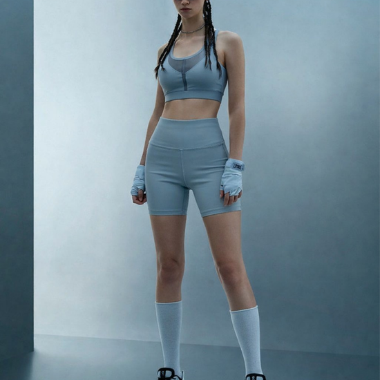 Person wearing a gray athletic outfit with sunglasses against a plain background