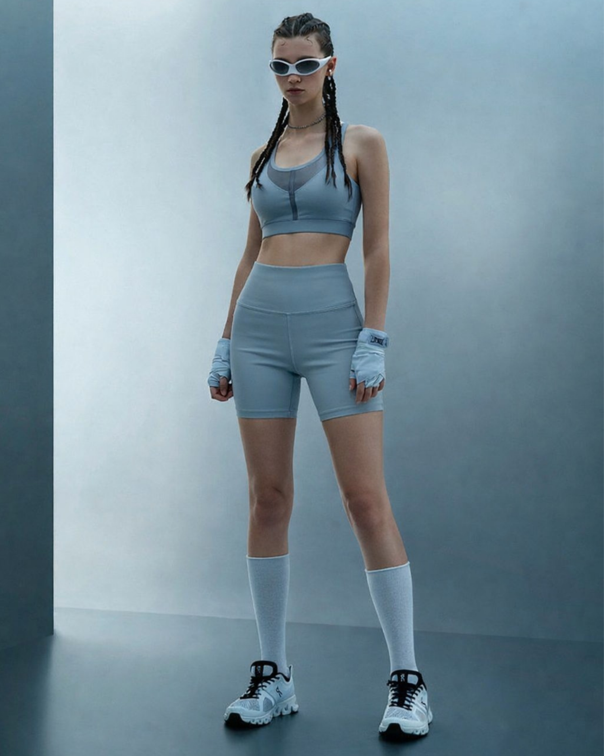 Person wearing a gray athletic outfit with sunglasses against a plain background