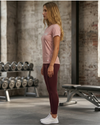 Woman in pink t-shirt and maroon leggings standing in a gym.