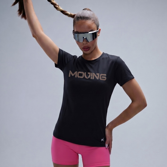 Person wearing a black 'MOVING' t-shirt and pink shorts with reflective sunglasses on a gray background