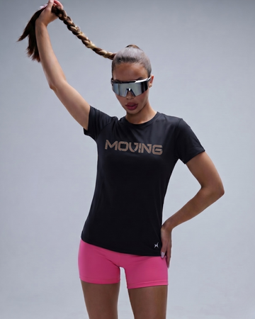 Person wearing a black 'MOVING' t-shirt and pink shorts with reflective sunglasses on a gray background