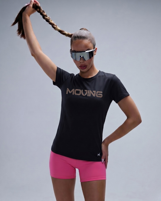 Person wearing a black 'MOVING' t-shirt and pink shorts with reflective sunglasses on a gray background