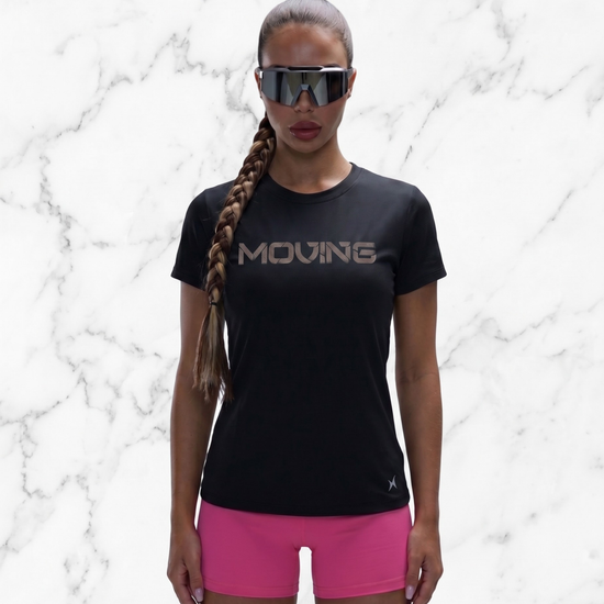 Person wearing a black 'MOVING' t-shirt and pink shorts against a marble background