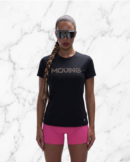 Person wearing a black 'MOVING' t-shirt and pink shorts against a marble background