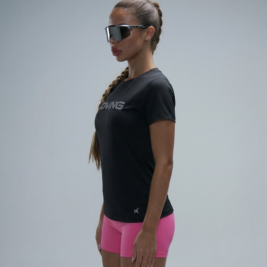 Woman wearing a black athletic shirt and pink shorts with sunglasses on a gray background