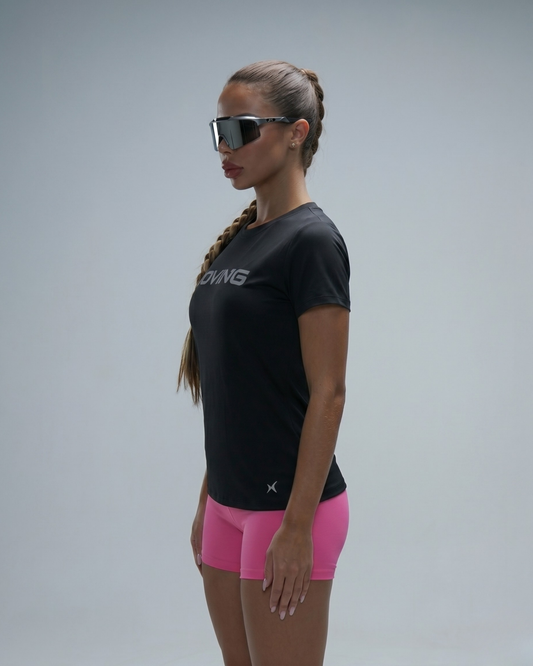 Woman wearing a black athletic shirt and pink shorts with sunglasses on a gray background