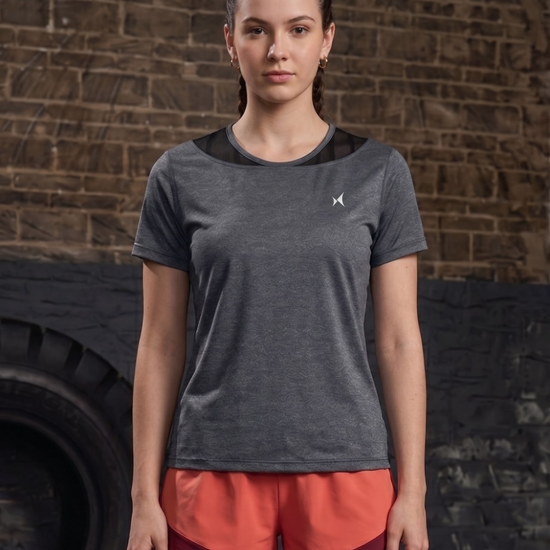 Woman wearing a gray athletic shirt and red shorts standing against a brick wall.