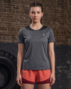 Woman wearing a gray athletic shirt and red shorts standing against a brick wall.
