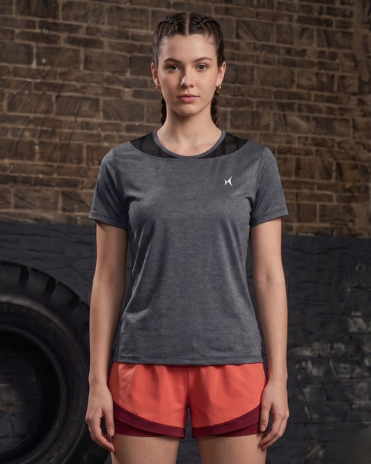 Woman wearing a gray athletic shirt and red shorts standing against a brick wall.