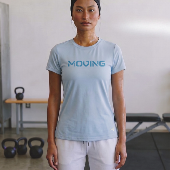 Person wearing a light blue 'MOVING' t-shirt in a gym setting