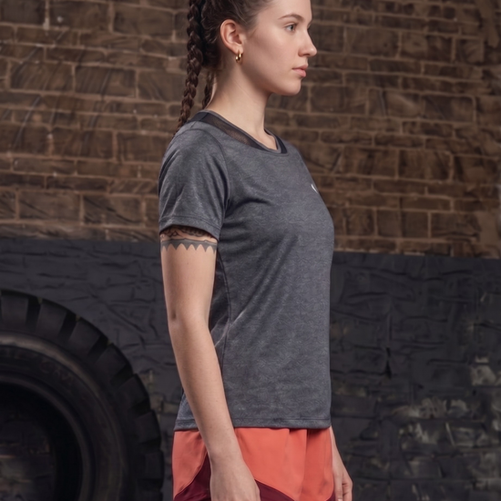 Woman in gray t-shirt and red shorts standing against a brick wall with a tire in the background