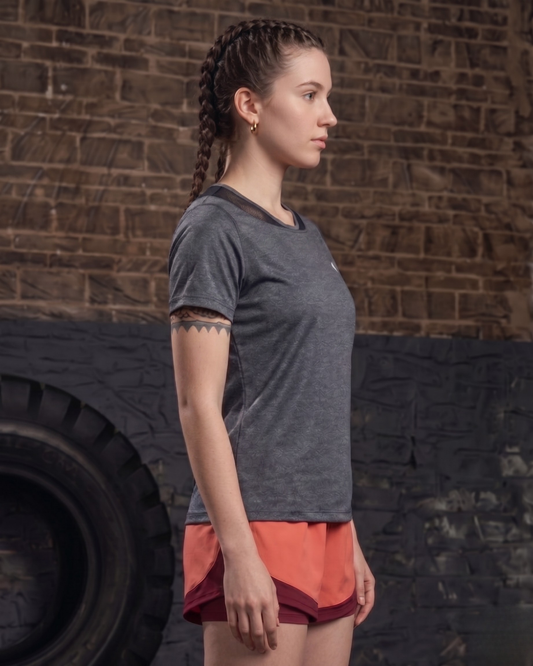 Woman in gray t-shirt and red shorts standing against a brick wall with a tire in the background