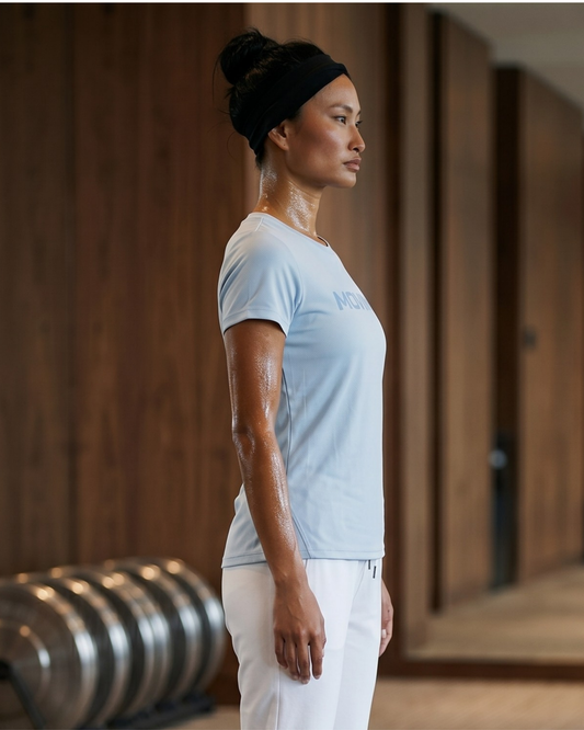 Woman in a light blue t-shirt and white pants standing in a yoga pose indoors.
