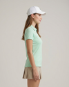 Woman wearing a light green polo shirt and beige skirt on a plain background