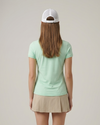 Person wearing a light green t-shirt and beige skirt with a white cap on a plain background