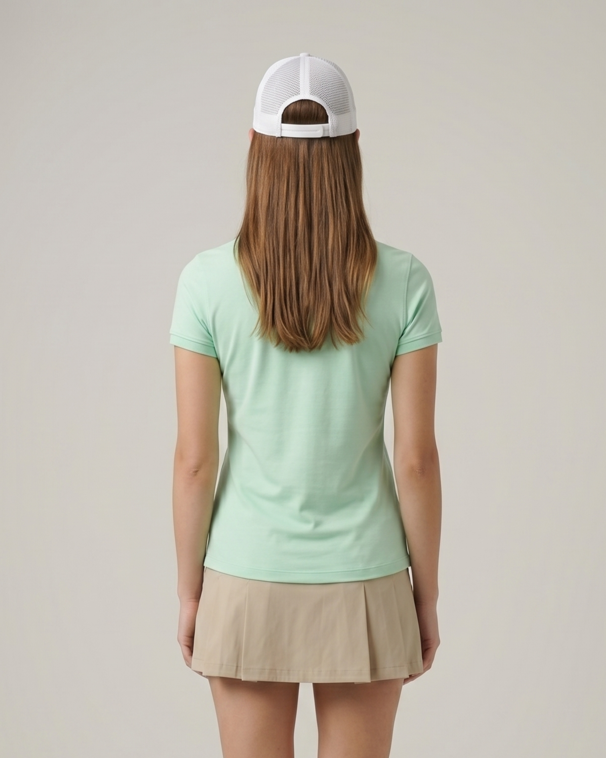 Person wearing a light green t-shirt and beige skirt with a white cap on a plain background