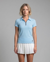 Woman wearing a light blue polo shirt and white skirt on a gray background