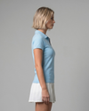 Woman wearing a light blue polo shirt and white skirt on a gray background