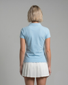 Person wearing a light blue polo shirt and white pleated skirt on a gray background