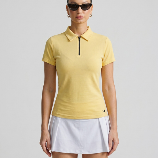 Woman wearing a yellow polo shirt and white skirt on a gray background