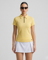 Woman wearing a yellow polo shirt and white skirt on a gray background