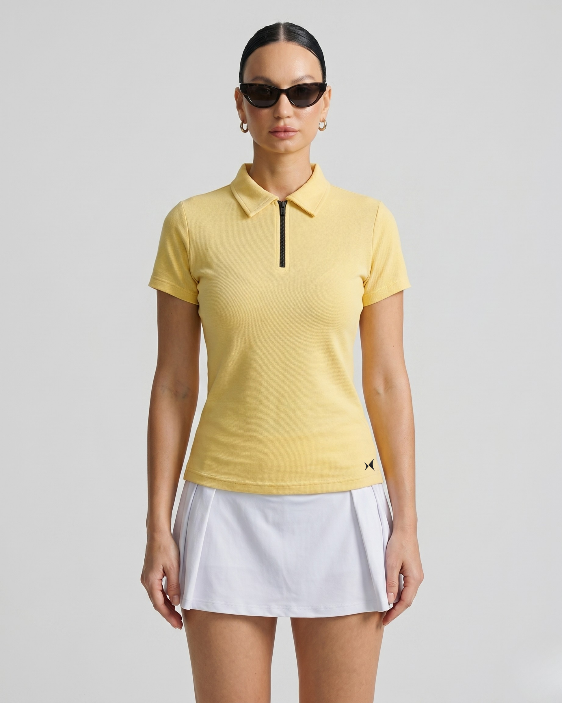 Woman wearing a yellow polo shirt and white skirt on a gray background