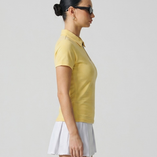 Woman wearing a yellow polo shirt and white skirt against a plain background
