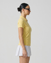 Woman wearing a yellow polo shirt and white skirt against a plain background