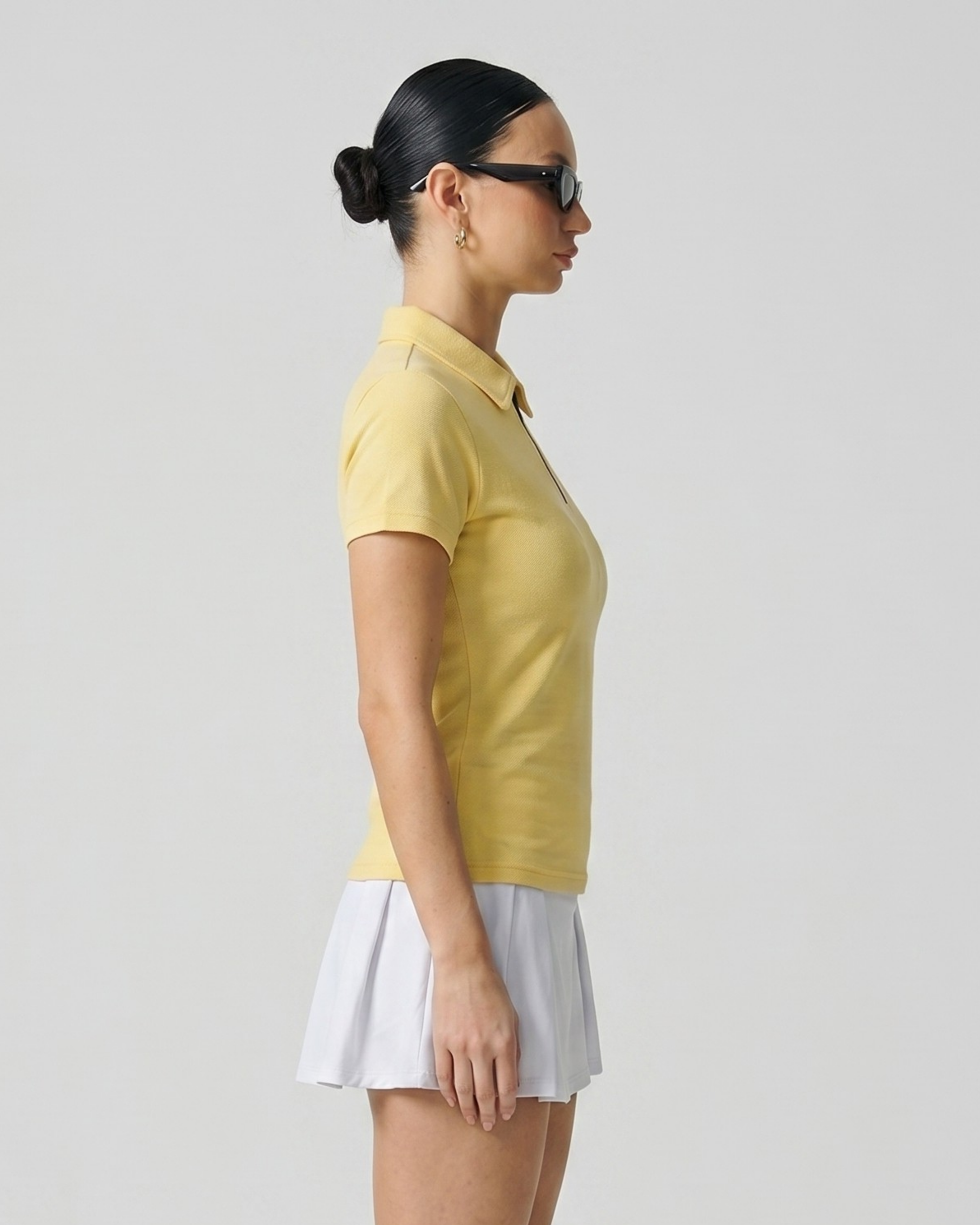 Woman wearing a yellow polo shirt and white skirt against a plain background
