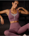 Woman wearing a purple sports bra and leggings sitting on a dark surface.