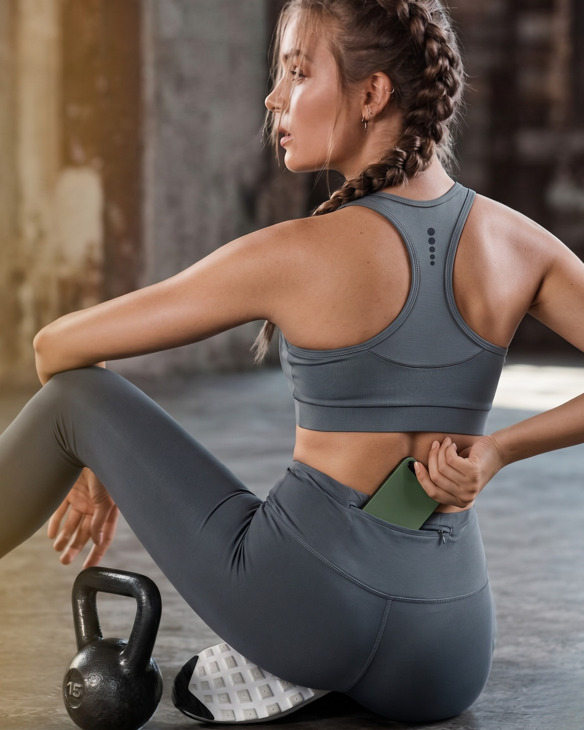 Woman in gray athletic wear stretching with a kettlebell on a wooden floor.