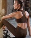 Woman in brown sports bra and leggings sitting on the floor with a kettlebell in a gym setting