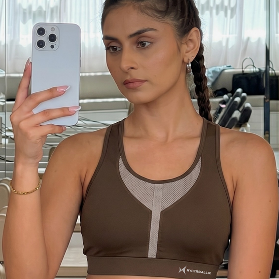 Woman taking a mirror selfie wearing a brown sports bra with a blurred background