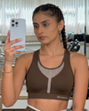 Woman taking a mirror selfie wearing a brown sports bra with a blurred background