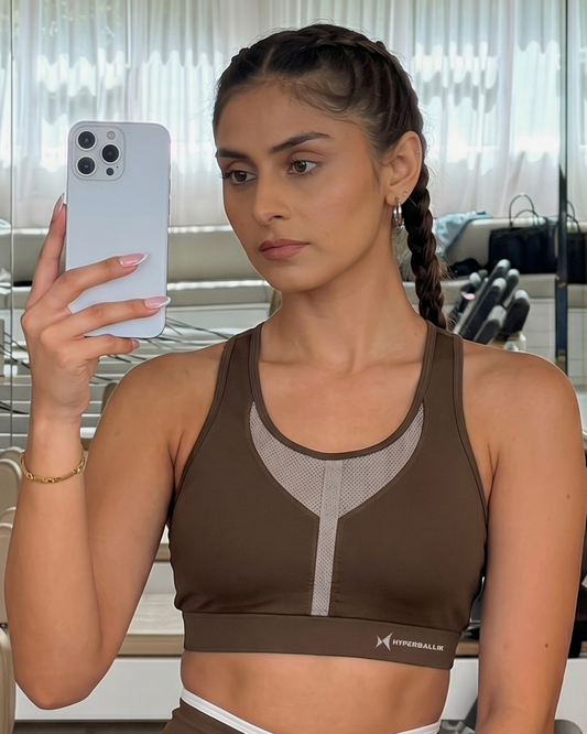Woman taking a mirror selfie wearing a brown sports bra with a blurred background