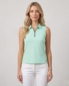 Woman wearing a light green sleeveless polo shirt and white pants on a plain background